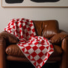 Bright red and white checkered pattern knitted cotton throw blanket styled in a brown leather chair