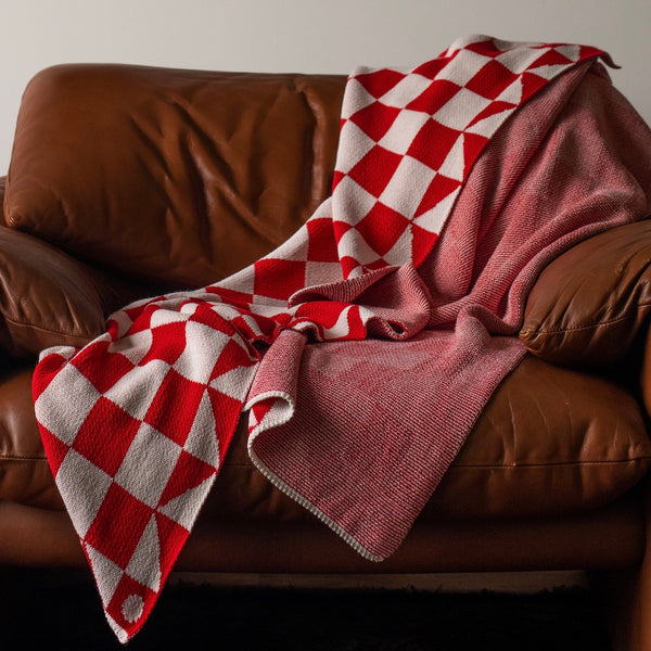 Bright red and white checkered pattern knitted cotton throw blanket styled in a brown leather chair